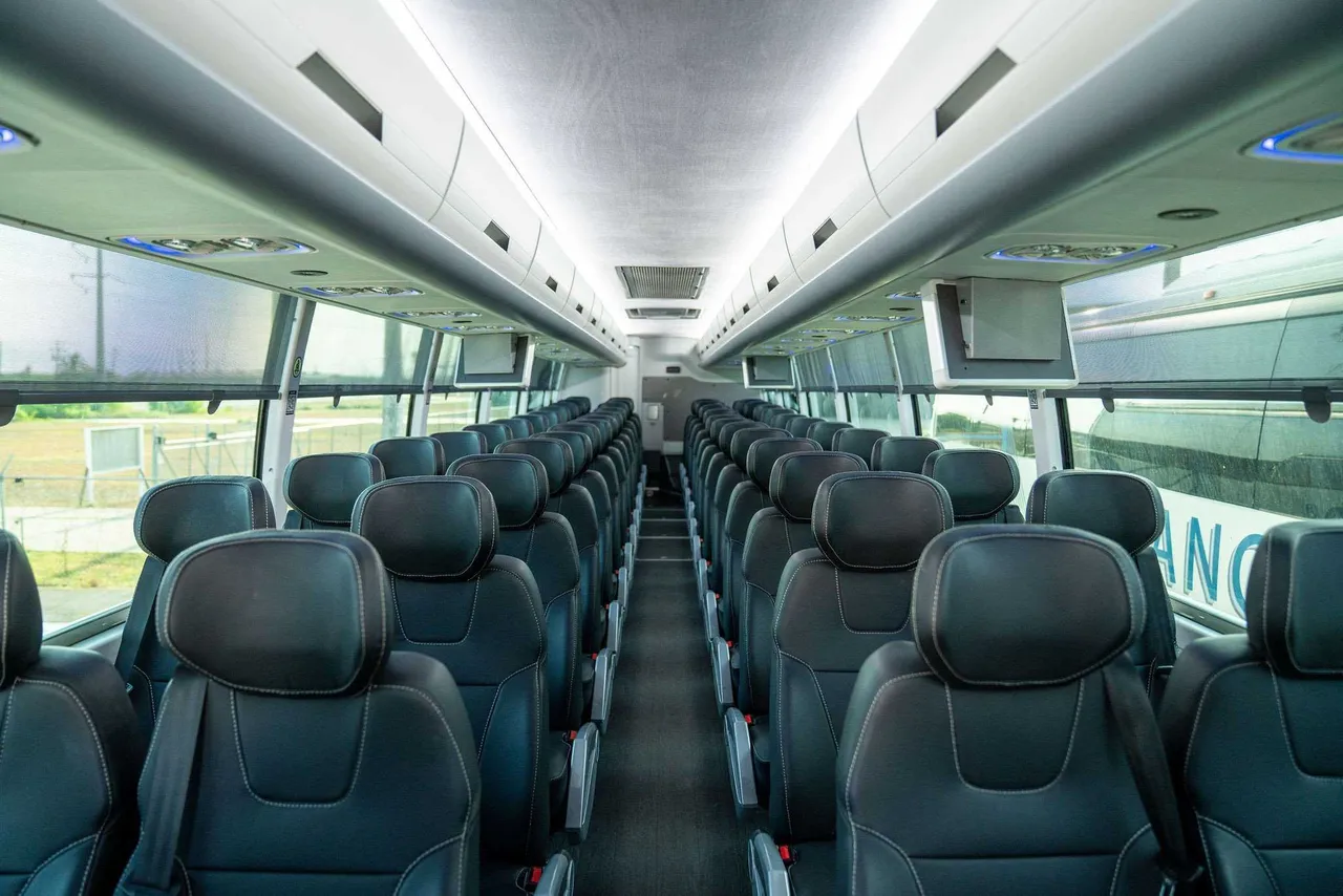 ADA Accessible Motorcoach cabin view with LED ceiling lighting, TV screens and overhead parcel racks